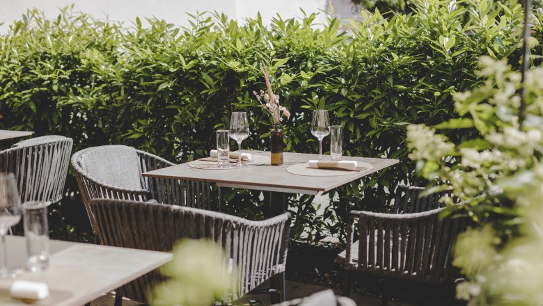 A cozy guest garden with covered tables and a green hedge in the background.