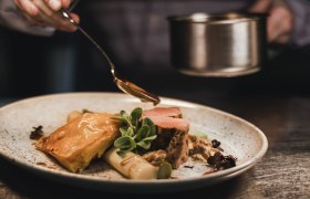 A plate of veal medallions, asparagus and puff pastry, garnished with sauce and herbs.