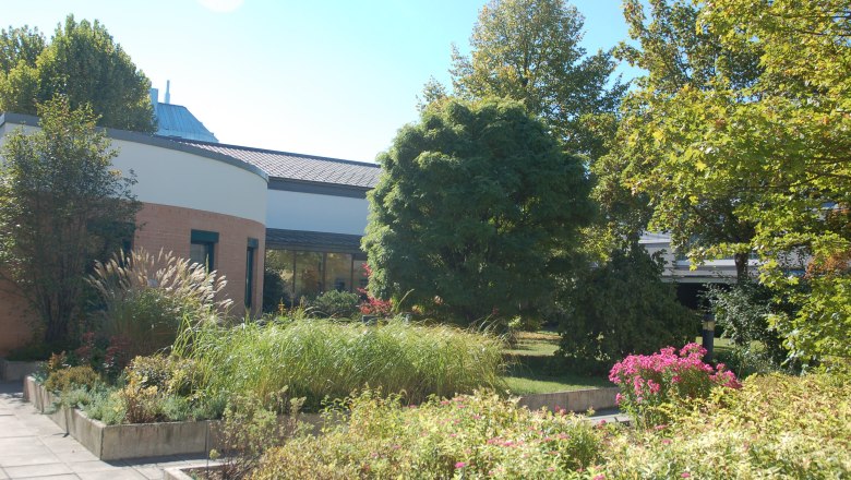 Garden of the Bildungshaus St. Hippolyt with plants and trees in front of a modern building.