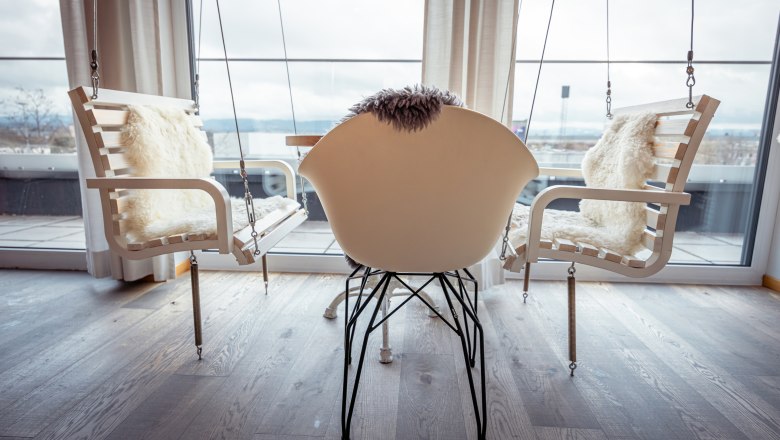 Innenraum mit Schaukelst&uuml;hlen und einem modernen Stuhl vor gro&szlig;en Fenstern.