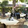 A cozy outdoor area of a café with tables, chairs and plants.